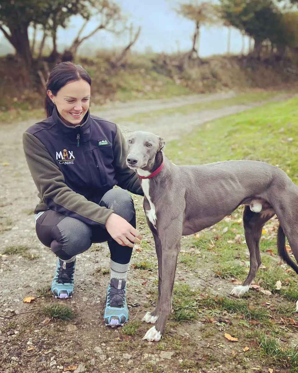 Emily Parton crouching beside a blue lurcher on a country lane
