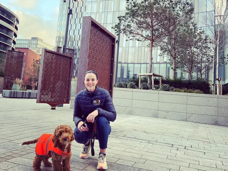 Emily with a cockapoo in a hi-vis coat in a city square